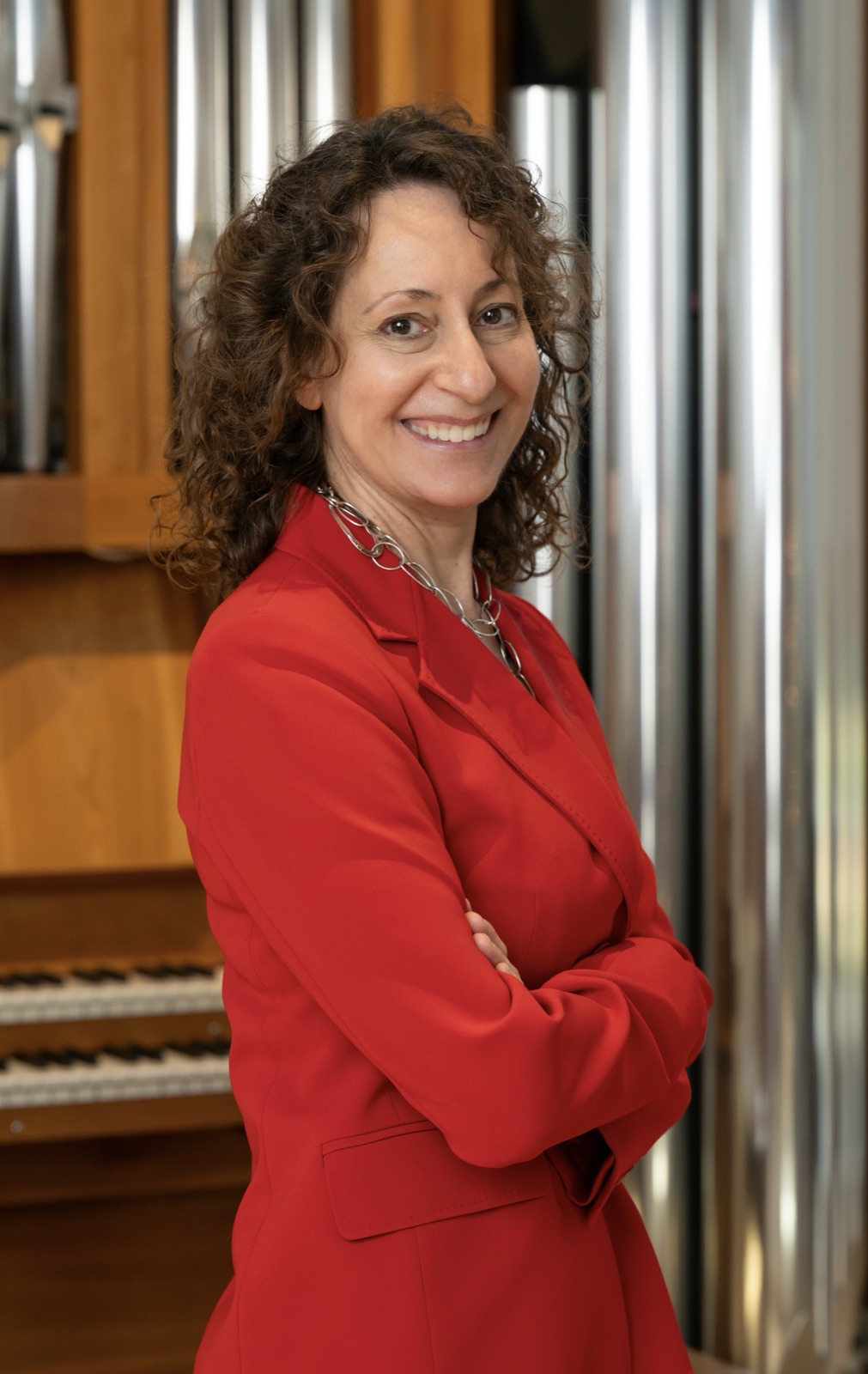 Sonja Kahler smiling in a red suit in front of pipe organ pipes